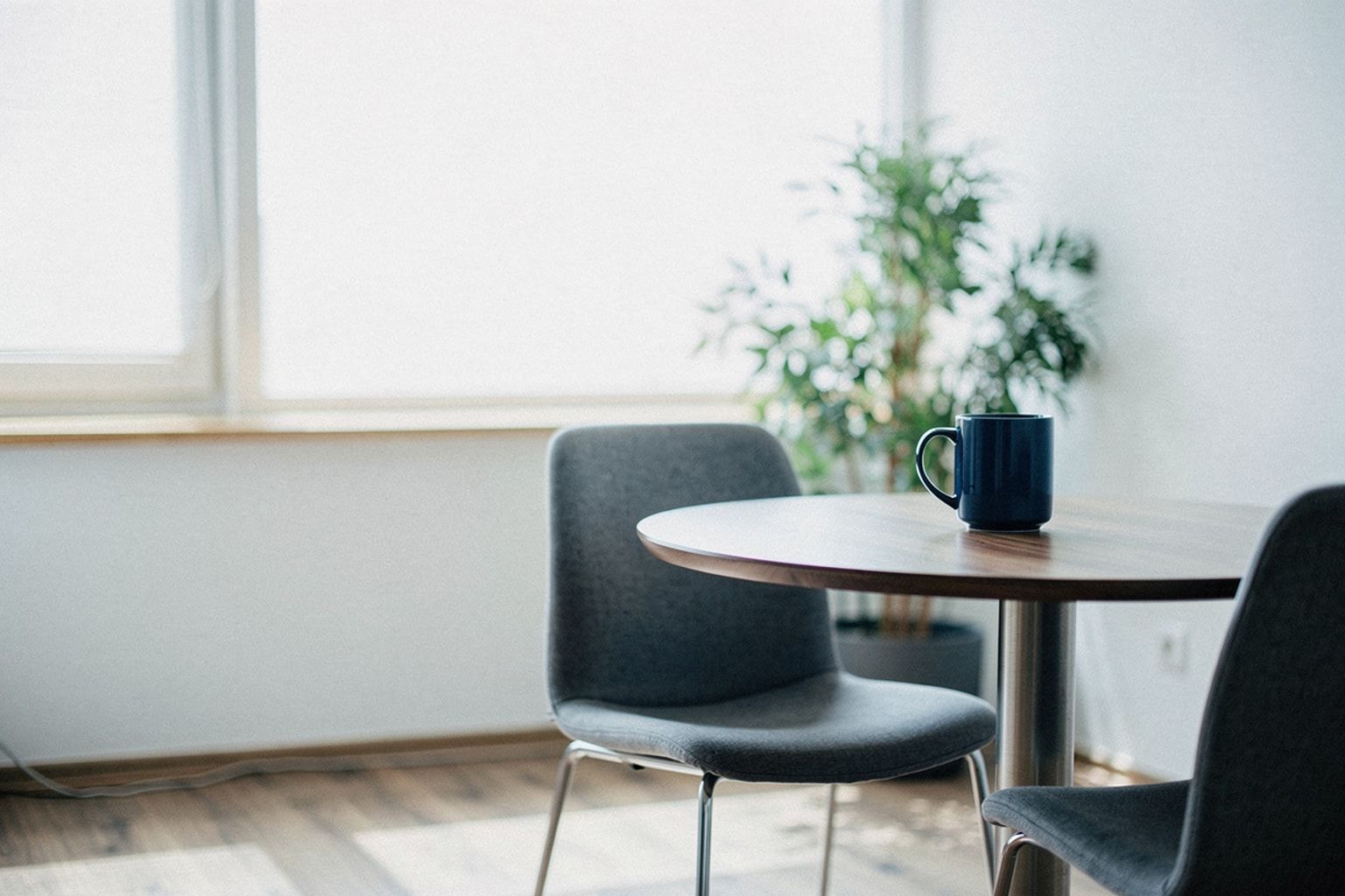 Kleiner runder Besprechungstisch mit zwei Stühlen am Fenster, darauf eine dunkelblaue Tasse